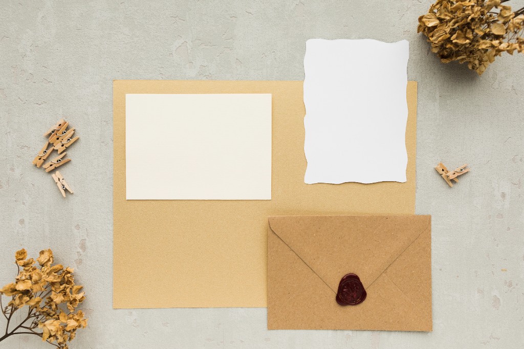 Invitation cards, envelope with wax seal, and dried flowers on a styled flat lay