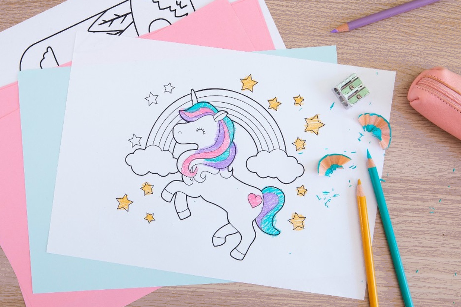 Top-down view of a partially colored unicorn page with pencils on a desk